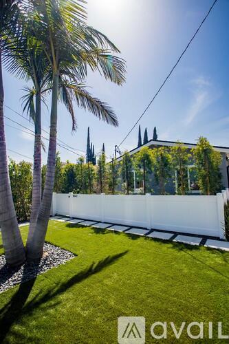 A sunny day with palm trees and a white fence in the foreground.