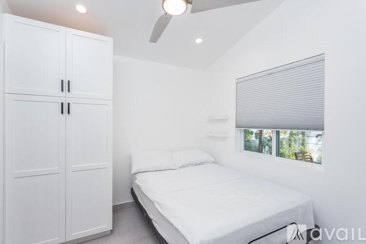 A white bedroom with a bed, a wardrobe, and a window with blinds.