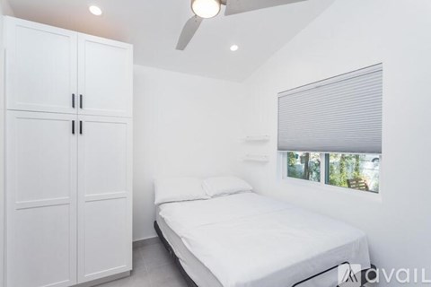 A white bedroom with a bed, a wardrobe, and a window with blinds.