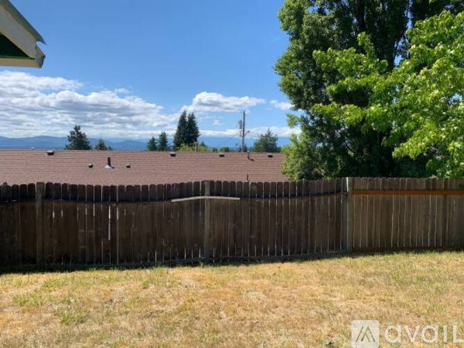 A wooden fence in front of a house with a tree and a mountain in the background.