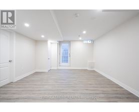A spacious room with wooden flooring and white walls, with a door leading to another room.
