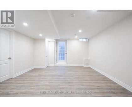 A spacious room with wooden flooring and white walls, with a door leading to another room.