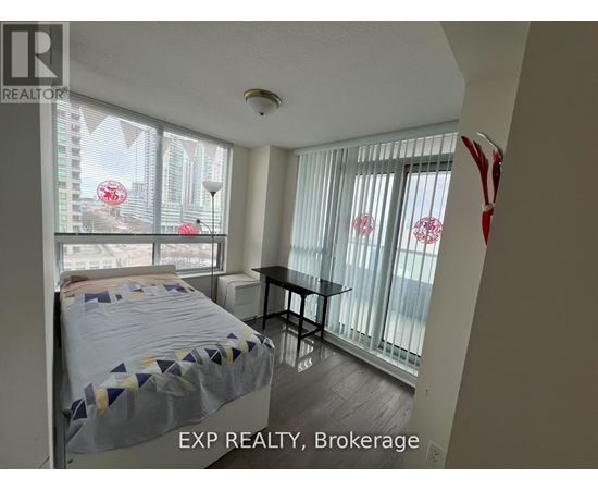 A bedroom with a bed, table, and a window with a view of a cityscape.