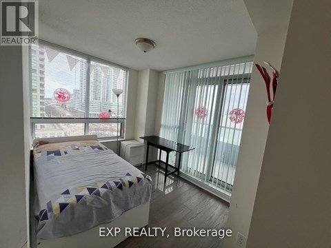 A bedroom with a bed, table, and a window with a view of a cityscape.