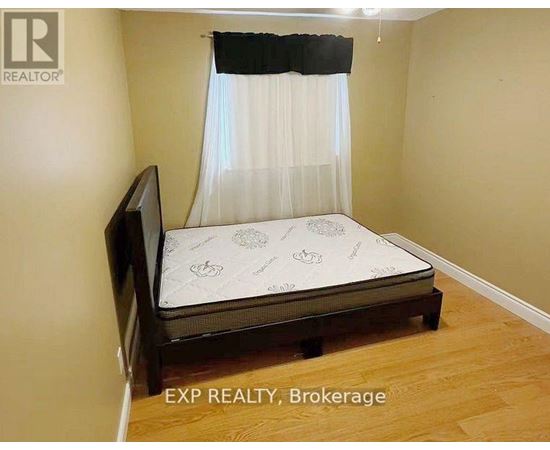 A bedroom with a bed, wooden headboard, and a white curtain.