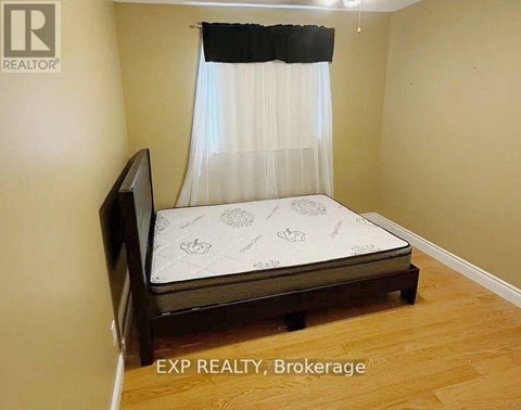 A bedroom with a bed, wooden headboard, and a white curtain.