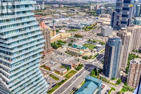 A cityscape with a mix of modern and older buildings, a large open space in the center, and a clear sky.