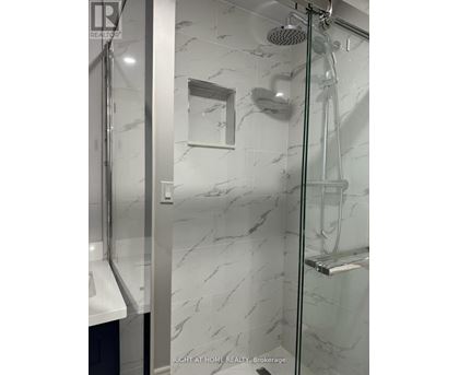 A shower with a marble wall and a glass door.