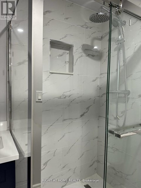 A shower with a marble wall and a glass door.