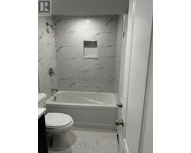 A white bathroom with a marble wall and a bathtub.