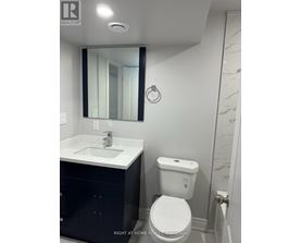 A white toilet with a blue dot on the lid is in a bathroom with a white sink and a mirror.