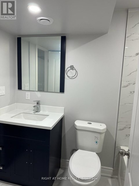A white toilet with a blue dot on the lid is in a bathroom with a white sink and a mirror.