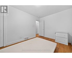 A white bedroom with a bed, dresser and nightstand.