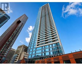 A tall building with a glass facade stands in front of other buildings on a sunny day.