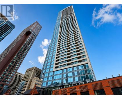 A tall building with a glass facade stands in front of other buildings on a sunny day.