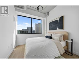 A bedroom with a large bed and a city view through the window.