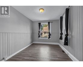 A spacious room with wooden flooring and white walls, featuring a window with black curtains and a coat rack with jackets.