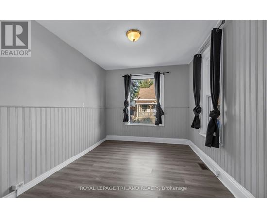 A spacious room with wooden flooring and white walls, featuring a window with black curtains and a coat rack with jackets.