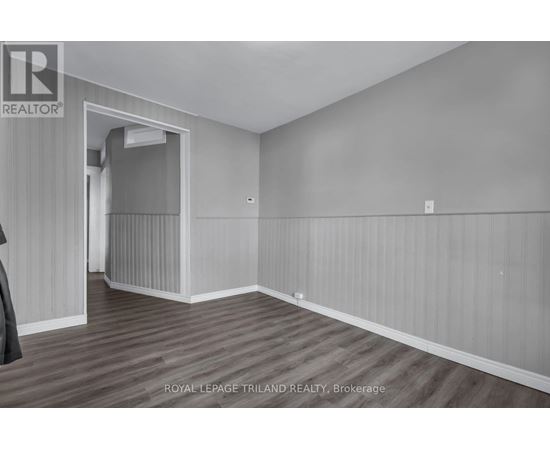 A room with wooden flooring and white walls, with a doorway leading to another room.