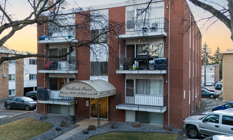 A red brick apartment building with a balcony and a sign that says Woodland Manor.