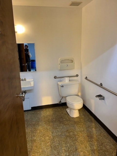 A white toilet with a white tank and a white sink in a bathroom.