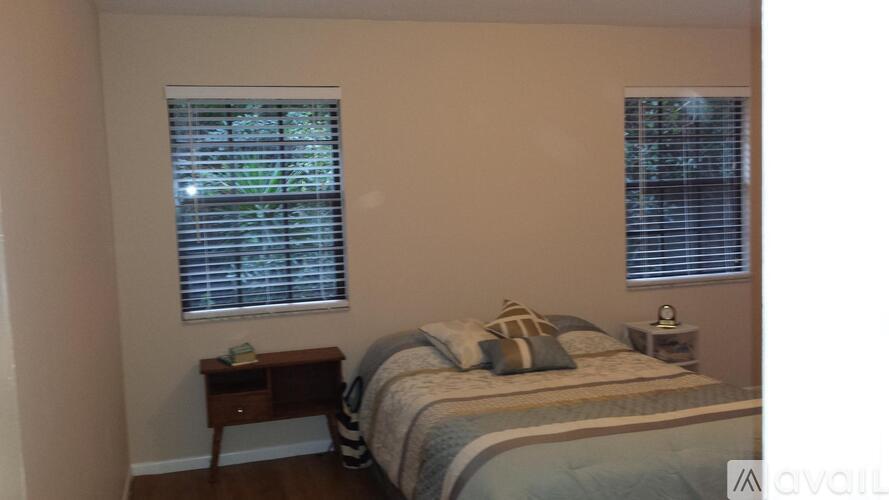 A bedroom with a bed, nightstand, and window with blinds.