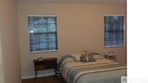 A bedroom with a bed, nightstand, and window with blinds.