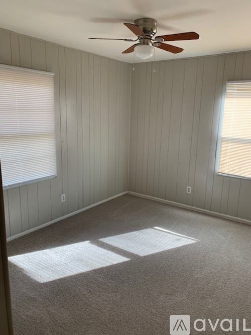 A room with a ceiling fan and two windows.