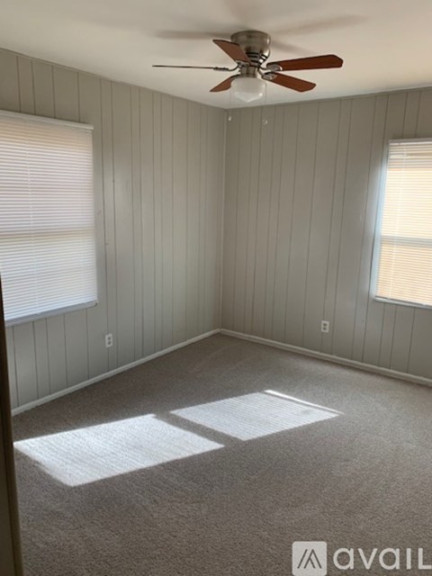 A room with a ceiling fan and two windows.