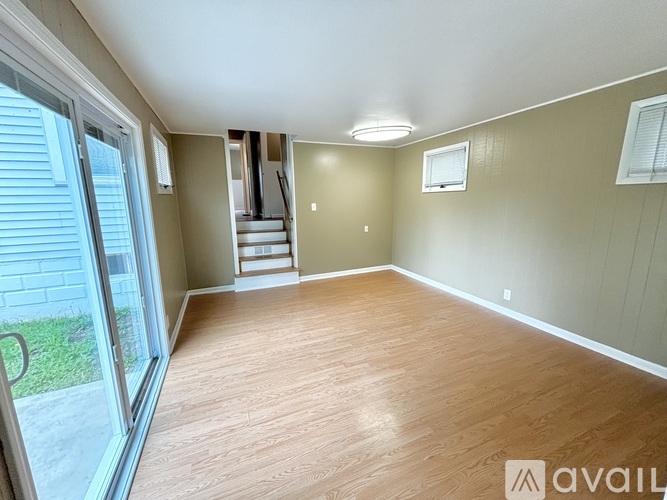 A spacious room with wooden flooring and a staircase in the background.