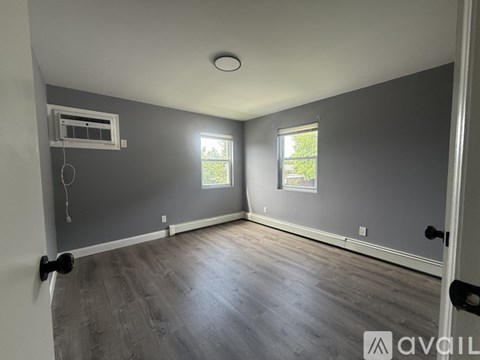 A room with grey walls and wooden flooring, featuring a window with a view of trees outside.