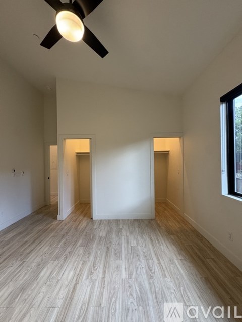 A room with a ceiling fan and light, wooden flooring, and a window with a view of trees outside.