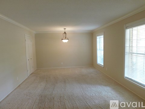 A room with a carpeted floor, a window with blinds, and a hanging light fixture.