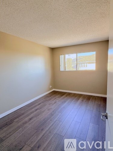 A room with wooden flooring and a window showing a building outside.