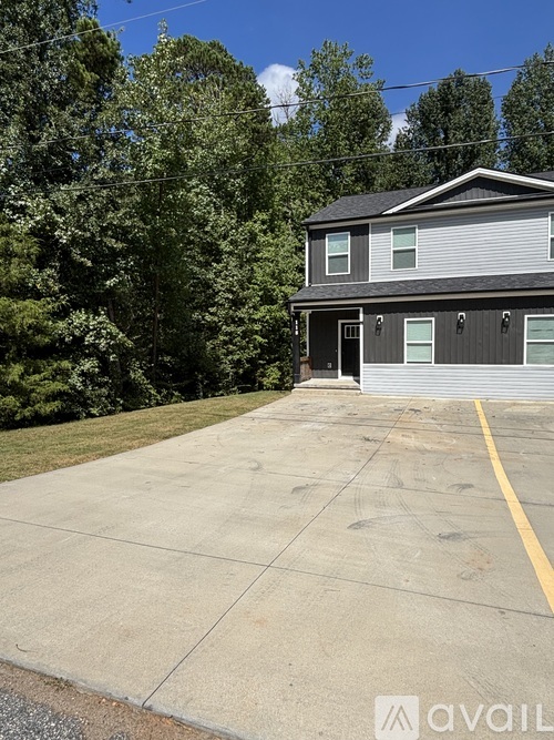 A house with a grey siding and a black roof is surrounded by trees.