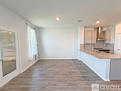 A spacious room with wooden flooring and a kitchen area in the background.