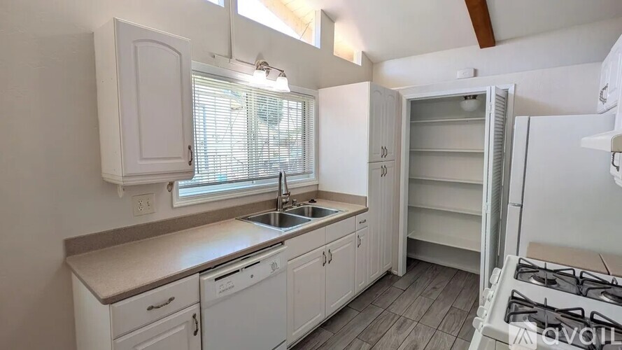 A kitchen with white cabinets and a window with blinds.