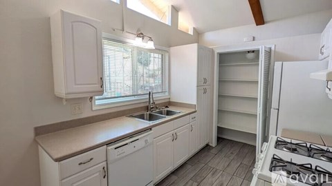 A kitchen with white cabinets and a window with blinds.