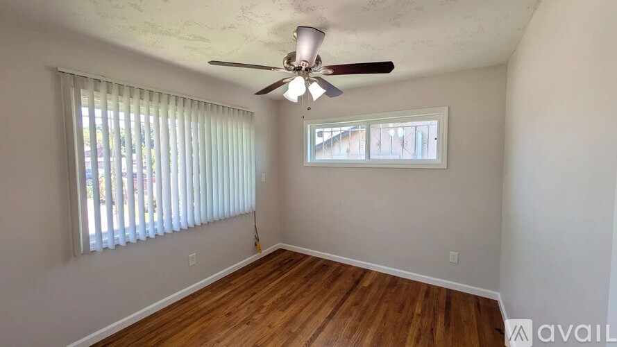 A room with a ceiling fan and two windows with blinds.