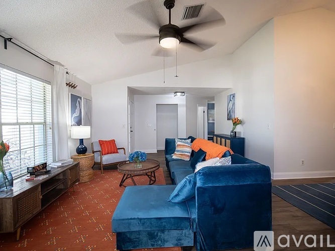 A living room with a blue velvet sofa and a fan on the ceiling.