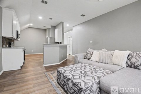 A modern living room with a grey sofa and a kitchen area in the background.
