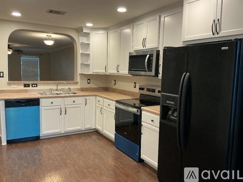 A black refrigerator is in the corner of a kitchen with white cabinets.