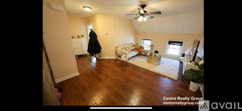 A woman in a black coat is walking through a spacious room with wood flooring and a ceiling fan.