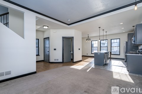 A spacious, empty living room with a kitchen area in the background.