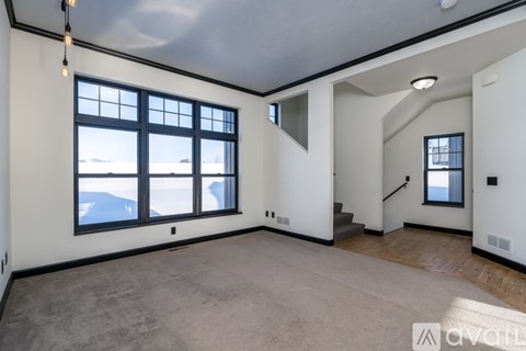 A spacious, empty room with large windows and a staircase.