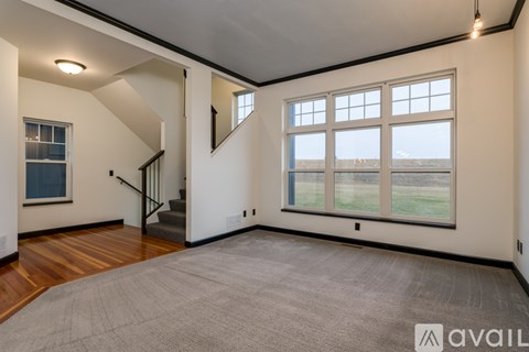 A spacious room with a carpeted floor, wooden stairs, and large windows overlooking a field.