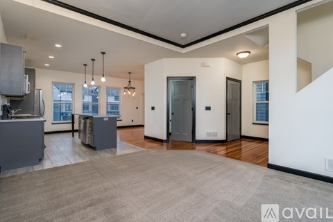 A spacious, well-lit living area with a kitchen on the left and a hallway leading to a bathroom on the right.