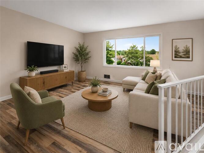 A living room with a green armchair, a white sofa, a wooden entertainment center, and a large window.