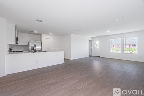 A spacious kitchen with white cabinets and a refrigerator, a dining area with a table and chairs, and a living area with a couch and a window.