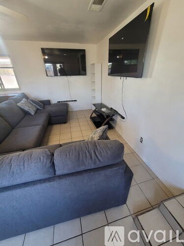 A living room with a grey couch and two TVs mounted on the wall.